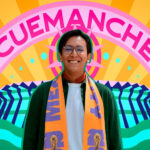 Photo of designer Mario Cortés smiling warmly, wearing glasses and an orange and purple FIFA Mexico City official scarf. The photo is set against a vibrant, stylized graphic background that features his artistic name, "CUEMANCHE," in large pink letters above a colorful sunburst design.