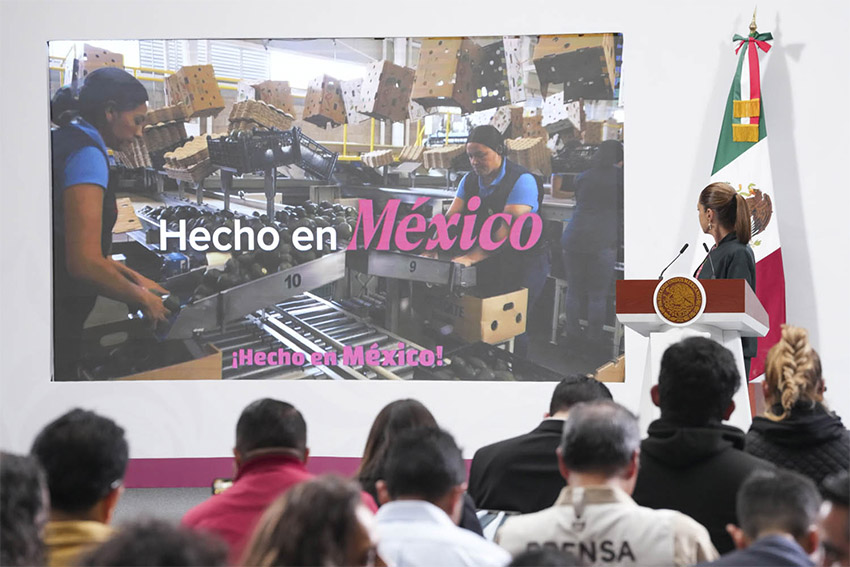 Sheinbaum looks at a projection showing Mexican workers with the words "Hecho en México" from the podium of her morning press conference