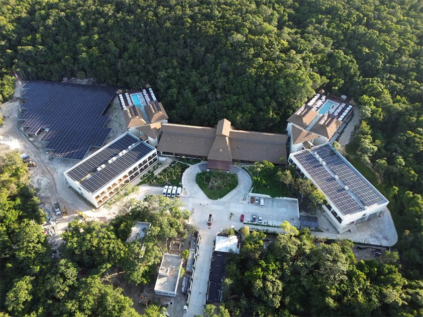 An aerial view of the government-owned hotel in Calakmul, showing a main building, covered parking, solar panels, gardens and two pools with views of the forest