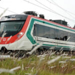 A red, white and green train speeds through a field.