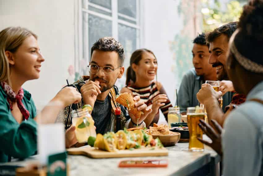 A diverse group of young expats and friends practice their Spanish conversation skills while enjoying tacos and drinks at a restaurant in Mexico.
