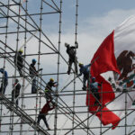Workers install scaffolding in front of a giant Mexican flag
