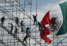Workers install scaffolding in front of a giant Mexican flag