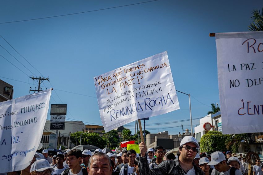 people hold up signs demanding Sinaloa Governor Rubén Rocha Moya resign at a peace march in Culiacán, the state capital