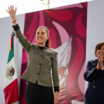 President Claudia Sheinbaum smiles and waves to a crowd from a stage