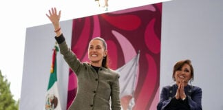 President Claudia Sheinbaum smiles and waves to a crowd from a stage