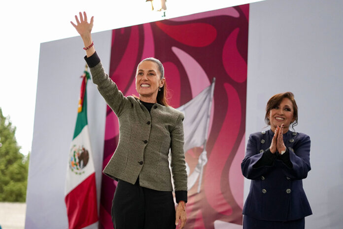 President Claudia Sheinbaum smiles and waves to a crowd from a stage