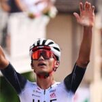 Isaac del Toro raises his hands in the air to celebrate winning a race