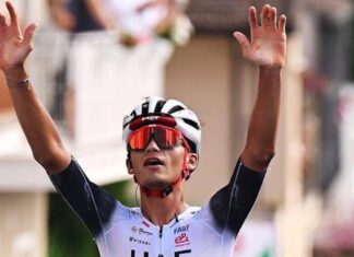 Isaac del Toro raises his hands in the air to celebrate winning a race