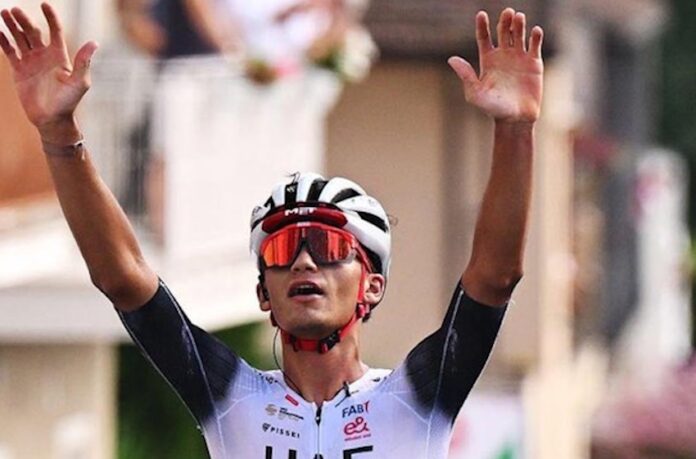 Isaac del Toro raises his hands in the air to celebrate winning a race