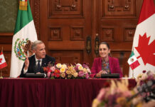 President Sheinbaum and Canada PM Mark Carney sit at a table in the National Palace with Canadian and Mexican flags