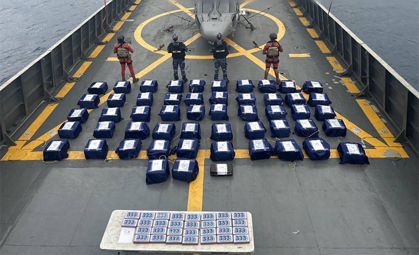 Navy officials guard packages of cocaine displayed on a ship's helicopter landing pad at sea
