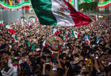 A man wearing a "Viva Mexico" sombrero wavves a giant Mexican flag in a packed crowd