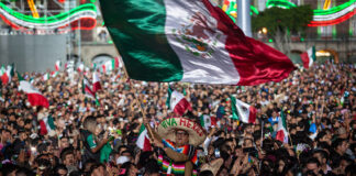 A man wearing a "Viva Mexico" sombrero wavves a giant Mexican flag in a packed crowd