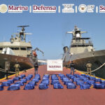 Navy sailors stand guard next to packages of cocaine, displayed between two navy ships