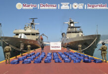 Navy sailors stand guard next to packages of cocaine, displayed between two navy ships