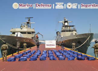 Navy sailors stand guard next to packages of cocaine, displayed between two navy ships