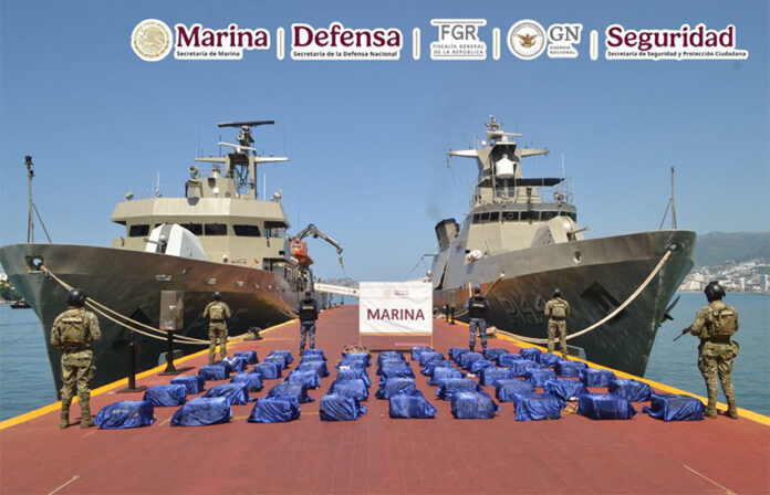 Navy sailors stand guard next to packages of cocaine, displayed between two navy ships