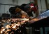 A masked person welds metal in an industrial workshop