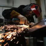 A masked person welds metal in an industrial workshop
