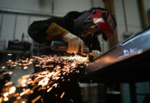 A masked person welds metal in an industrial workshop