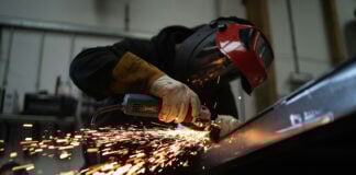 A masked person welds metal in an industrial workshop