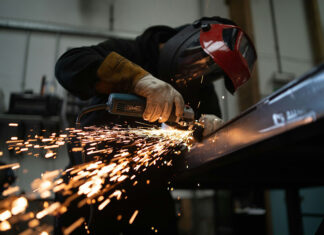 A masked person welds metal in an industrial workshop