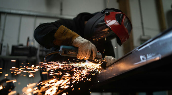 A masked person welds metal in an industrial workshop