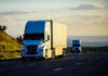 Two trucks or semi-trailers drive down a highway, possibly carrying Mexican exports to the US