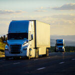 Two trucks or semi-trailers drive down a highway, possibly carrying Mexican exports to the US