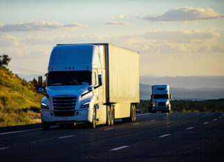 Two trucks or semi-trailers drive down a highway, possibly carrying Mexican exports to the US