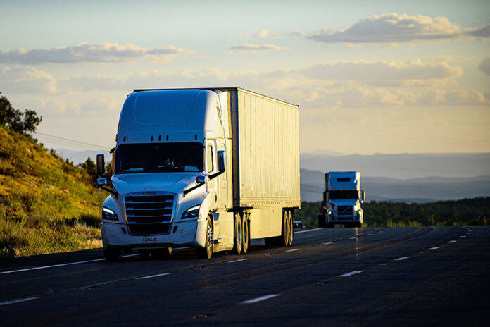 Two trucks or semi-trailers drive down a highway, possibly carrying Mexican exports to the US