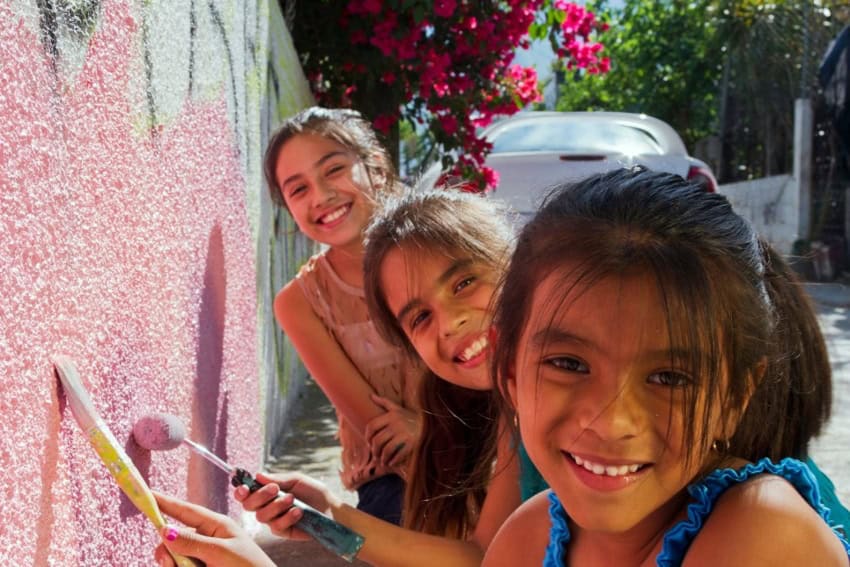 Girls painting an exterior wall with Comex paint.