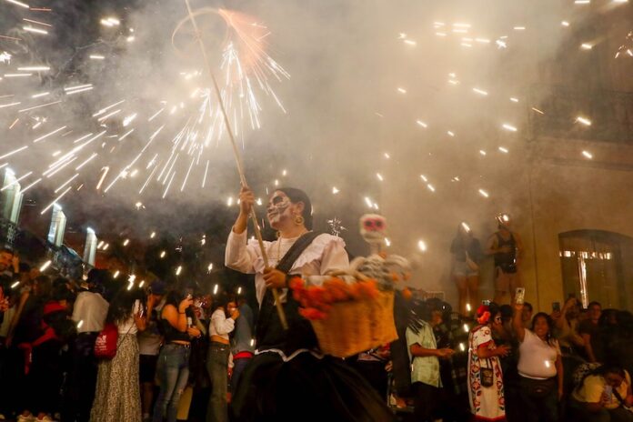 Participants of Oaxaca's Day of the Dead parade with fireworks in the background