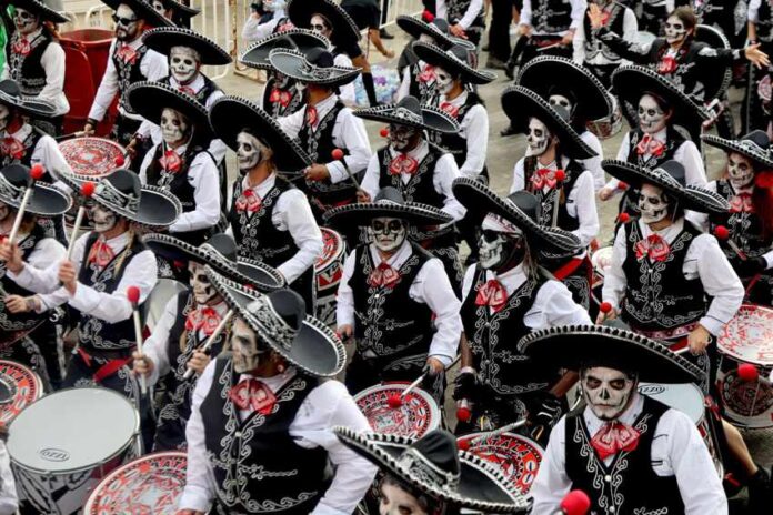 Gran desfile de Día de Muertos 2024 A large marching band performs in a Día de los Muertos parade in Mexico City, dressed in black mariachi-style outfits with sombreros and their faces painted as calaveras, or skulls.