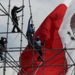 workers on scaffolding in front of a Mexican flag
