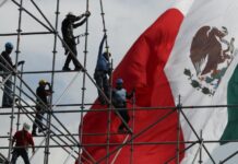 workers on scaffolding in front of a Mexican flag
