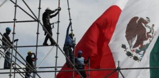 workers on scaffolding in front of a Mexican flag