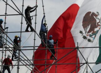 workers on scaffolding in front of a Mexican flag