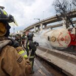 Firefighters hose down a gas tanker on its side in a highway