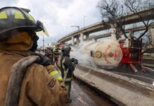 Firefighters hose down a gas tanker on its side in a highway