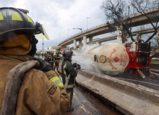 Firefighters hose down a gas tanker on its side in a highway