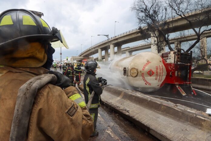 Firefighters hose down a gas tanker on its side in a highway