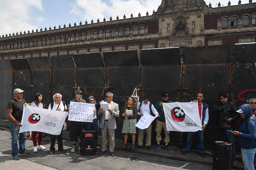 People hold signs and banners in front of the National Palace, which is surrounded by metal barricades