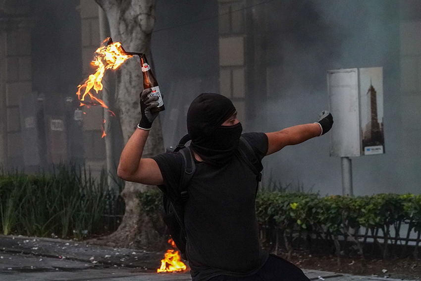 A protester dressed in black wearing a balaclava throws a molotov cocktail.