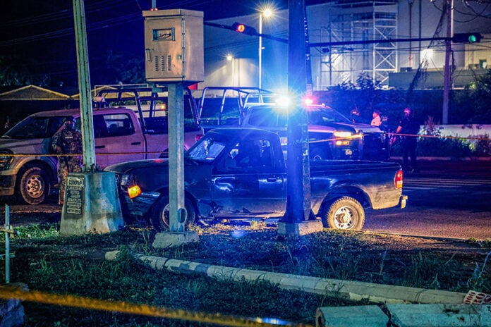 Police cars with lights flashing surround a damaged car crashed into a pole at night in Culiacán, Sinaloa