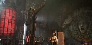 A movie still from Guillermo del Toro's film "Frankenstein" shows actor Oscar Isaac as Victor Frankenstein in his palatial gothic laboratory, staring upward at the ceiling, surrounded by equipment made of wood and brass.