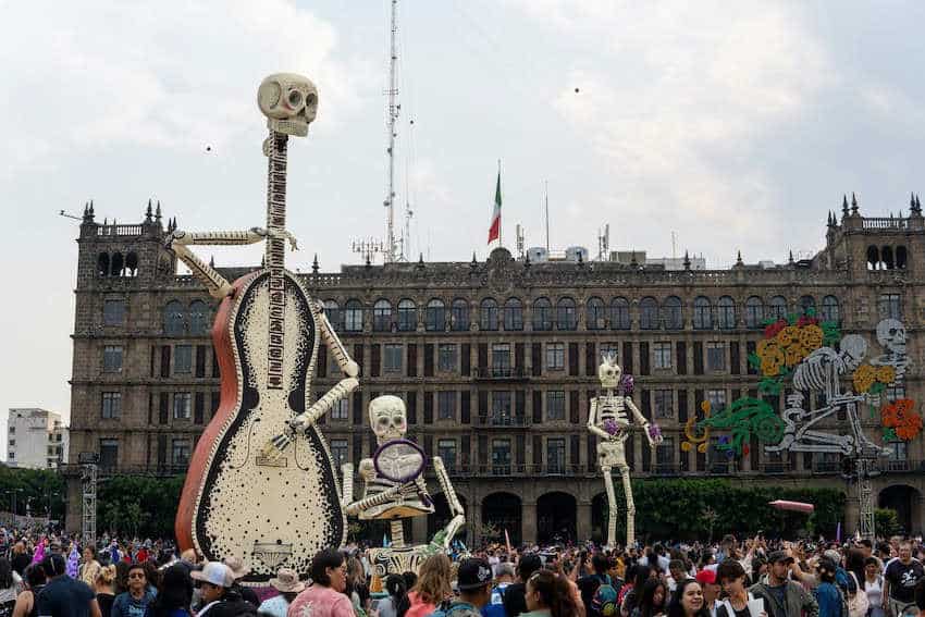 Giant skeleton figures (calacas), including 1  shaped similar  a guitar, operation    implicit    a ample  assemblage  successful  Mexico City's Zócalo square, with the National Palace successful  the background, during a Day of the Dead celebration.