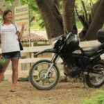 A woman in a white t-shirt stands next to a black touring motorcycle