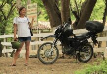 A woman in a white t-shirt stands next to a black touring motorcycle